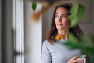 Ways to be more eco-friendly, woman looking out of nearby window, with cup of coffee in hands